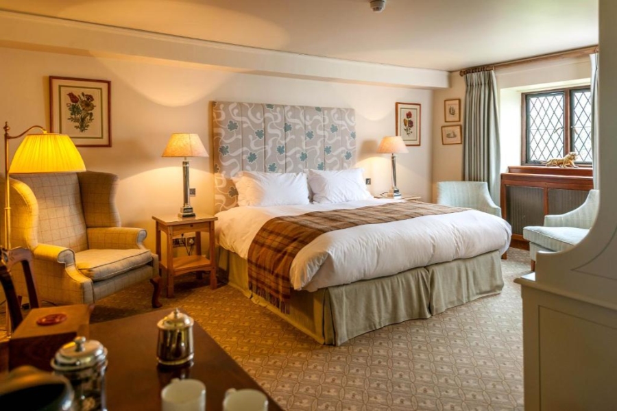 Interior of a hotel room at Amberley Castle, highlighting a bed, a chair, and a lamp in a refined setting.