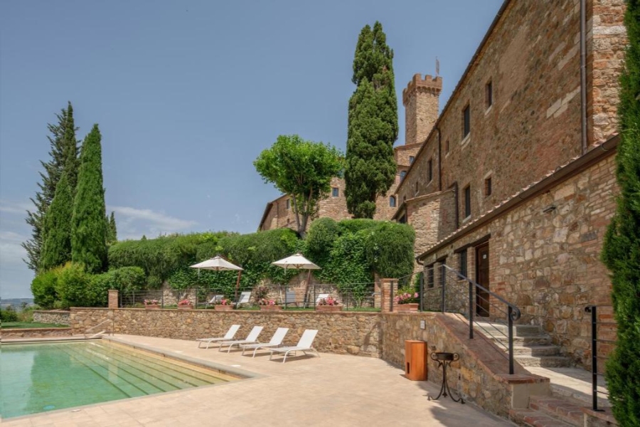 The villa's pool at Castello Banfi Il Borgo is framed by lush trees, creating a serene outdoor retreat in Italy.