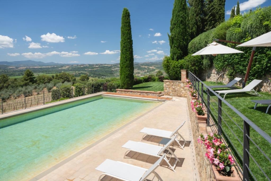 Tranquil poolside scene featuring lawn chairs, overlooking a lush hillside at Castello Banfi Il Borgo, Italy.