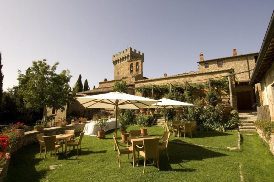 The exterior of Castello di Gargonza, featuring a garden area with tables and chairs for outdoor seating.