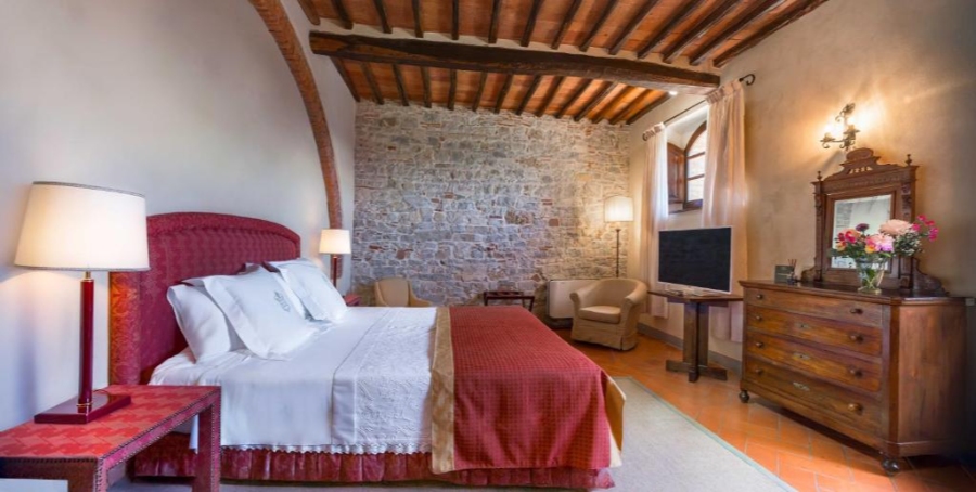 Elegant bedroom with a striking red headboard against a textured stone wall, showcasing a blend of comfort and style.