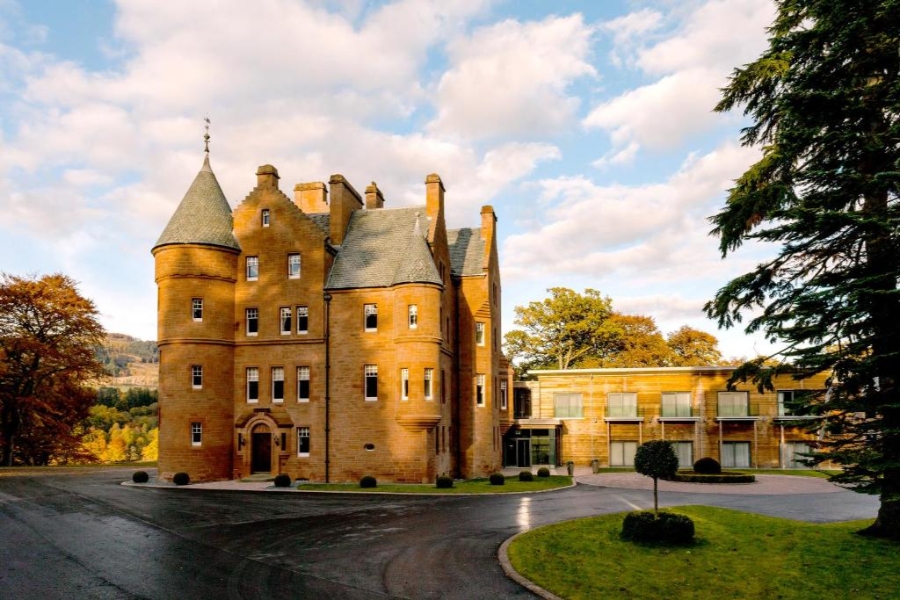Fonab Castle Hotel & Spa, a historic castle surrounded by lush trees and green grass in the United Kingdom.