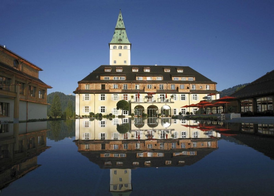 The Schloss Elmau Luxury Retreat showcases a prominent clock tower and a serene pool area amidst scenic landscapes.