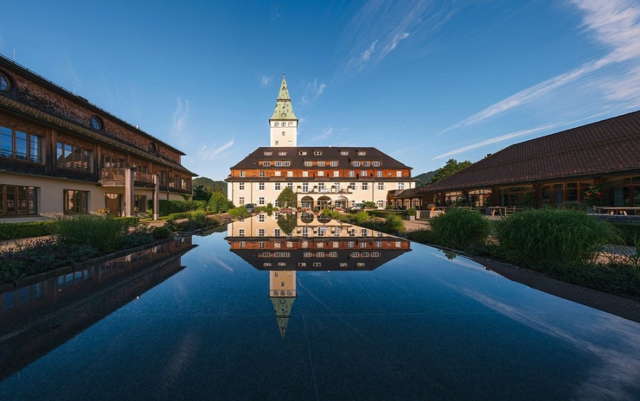 Courtyard of Schloss Elmau Luxury Retreat featuring a prominent clock tower amidst elegant architecture and lush greenery.