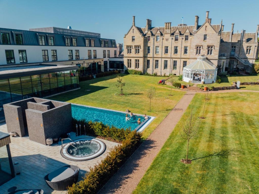 The swimming pool at Schloss Roxburghe Golf Resort is depicted, with a lush lawn area providing a serene environment for guests.