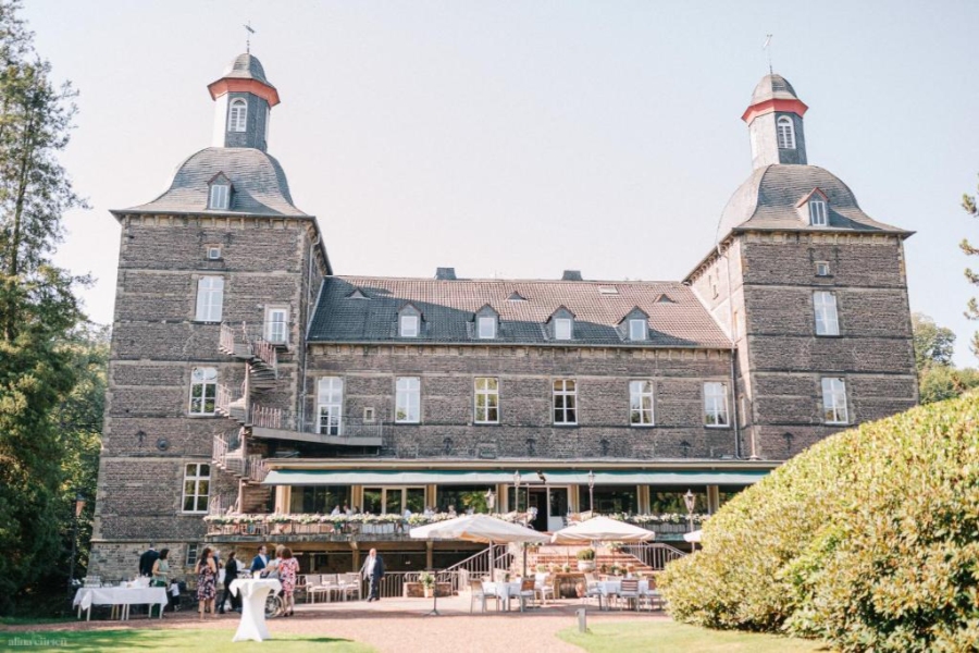Guests celebrate a wedding outside the elegant Schlosshotel Hugenpoet, showcasing the castle's stunning architecture and gardens.