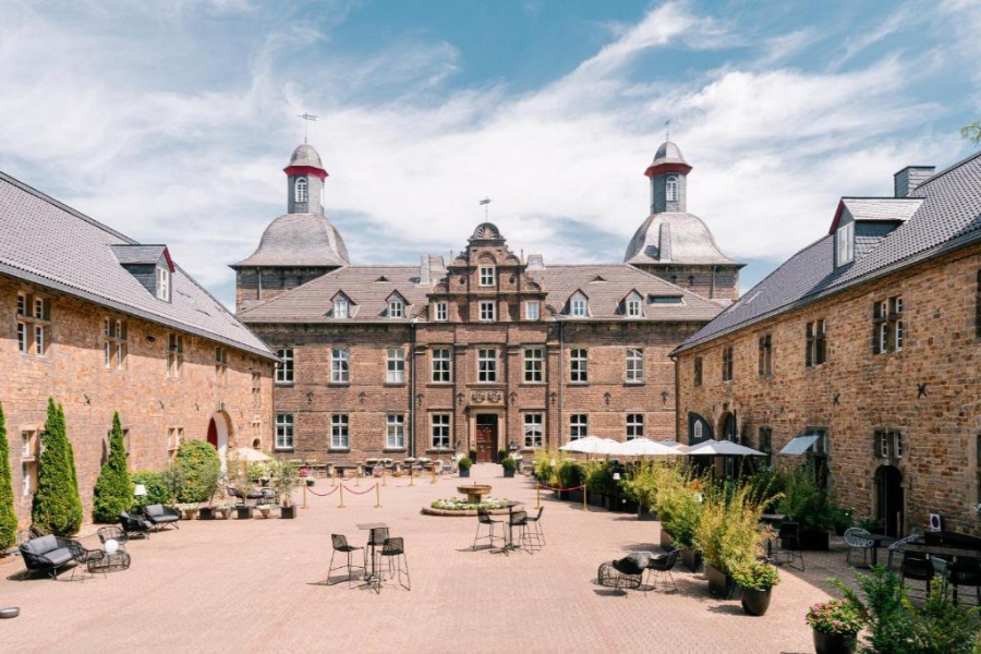 Scenic view of the castle courtyard at Schlosshotel Hugenpoet, showcasing the grand architecture and lush surroundings.